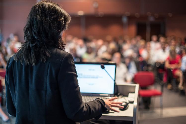 Female speaker giving a talk on corporate business conference. Unrecognizable people in audience at conference hall. Business and Entrepreneurship event. By kasto